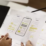 Hands holding a paper with three mobile app wireframe design sketches