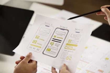 Hands holding a paper with three mobile app wireframe design sketches