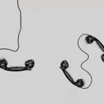 Two old-fashioned black telephone handsets with cords placed on a light gray background, symbolizing broken or unclear communication, and representing communication between IT and business