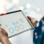 Pessoa segurando tablet com painel de analytics e gráficos de desempenho, representando como testar sistemas ERP