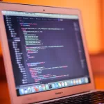 Notebook MacBook Air com código de programação colorido aberto na tela.