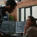 Dois profissionais de TI conversando em frente a monitores com códigos de programação em um escritório moderno.