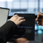 Dois profissionais de tecnologia trabalhando em conjunto, visualizando código de programação em laptop com ambiente de desenvolvimento integrado