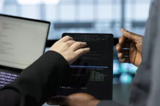 Dois profissionais de tecnologia trabalhando em conjunto, visualizando código de programação em laptop com ambiente de desenvolvimento integrado