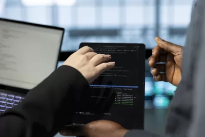 Dois profissionais de tecnologia trabalhando em conjunto, visualizando código de programação em laptop com ambiente de desenvolvimento integrado