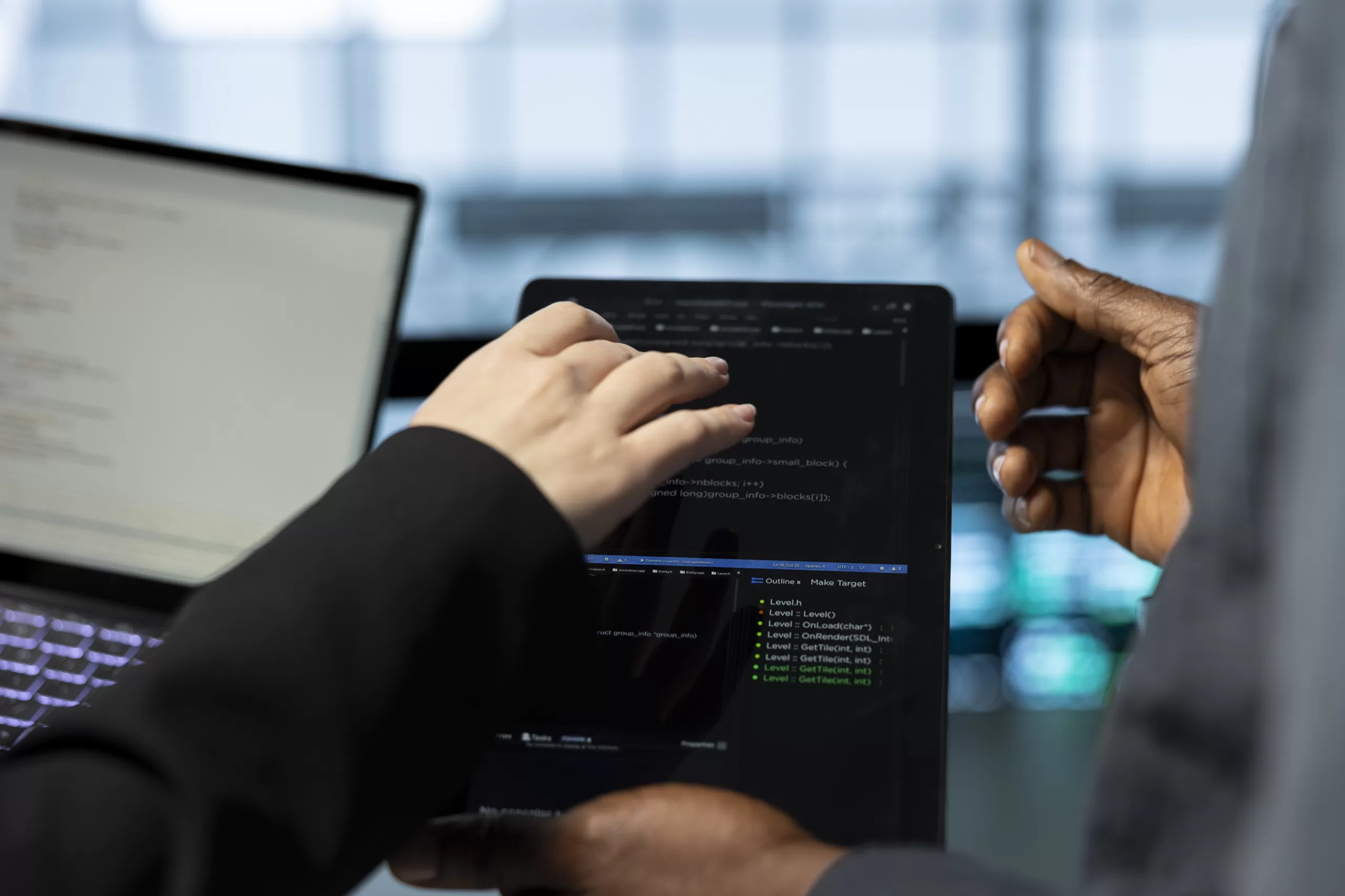 Dois profissionais de tecnologia trabalhando em conjunto, visualizando código de programação em laptop com ambiente de desenvolvimento integrado