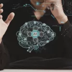 Close-up de uma pessoa com as mãos gesticulando ao redor de uma ilustração digital de um cérebro humano estilizado com circuitos eletrônicos. No centro do cérebro, há um ícone com o texto "AI", cercado por gráficos de conexões tecnológicas em tons de azul.