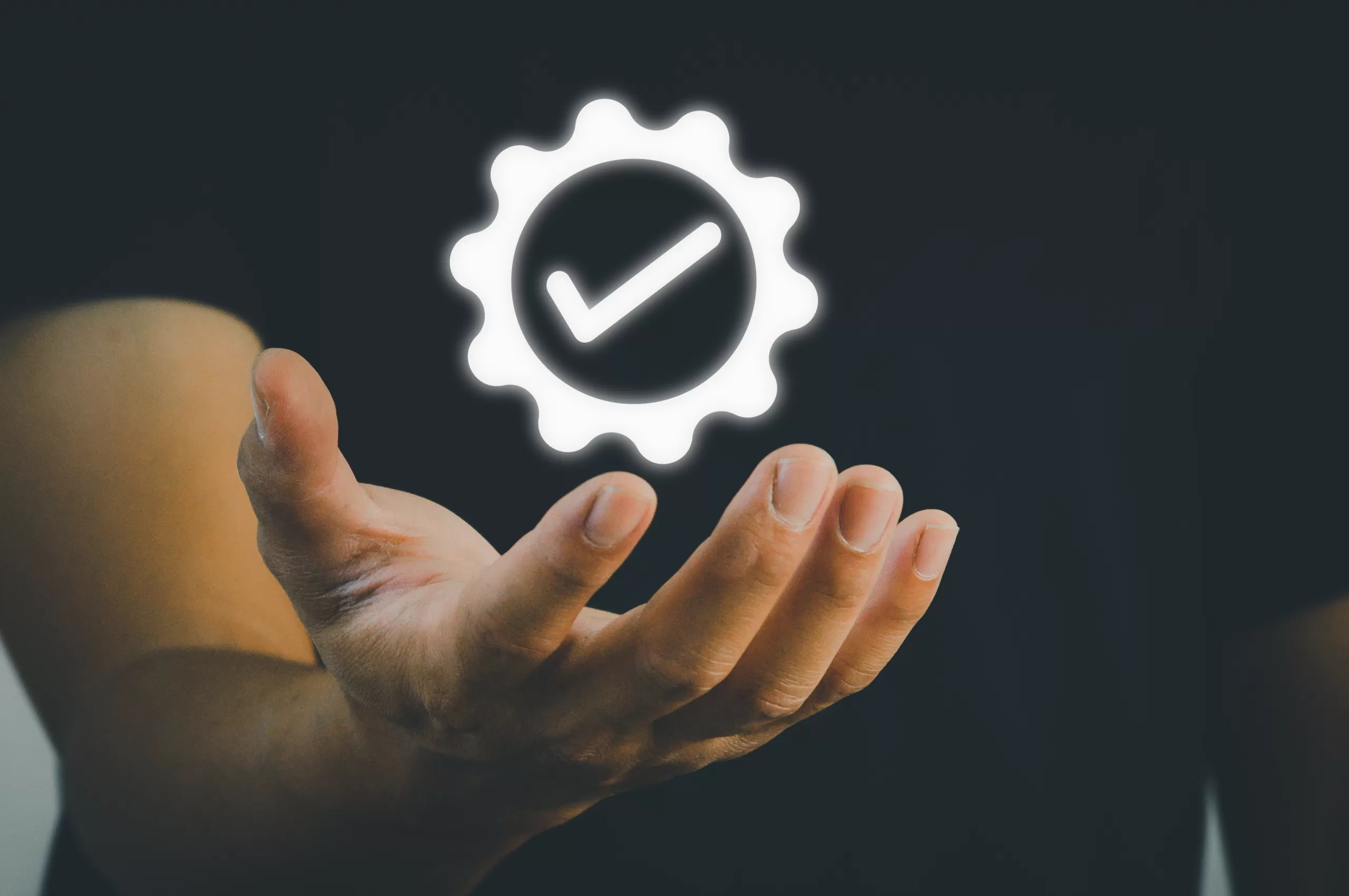Mão aberta sustentando um ícone luminoso de engrenagem com símbolo de aprovação, representando qualidade assegurada e certificação em processos de software.